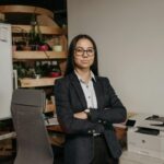 Confident woman in business attire standing in modern office with arms crossed.